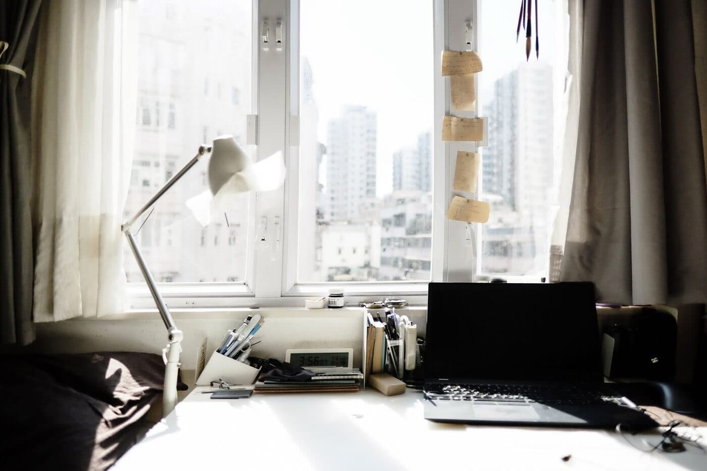 A tidy home-office desk with a laptop, notebook and a mug near a sunny window