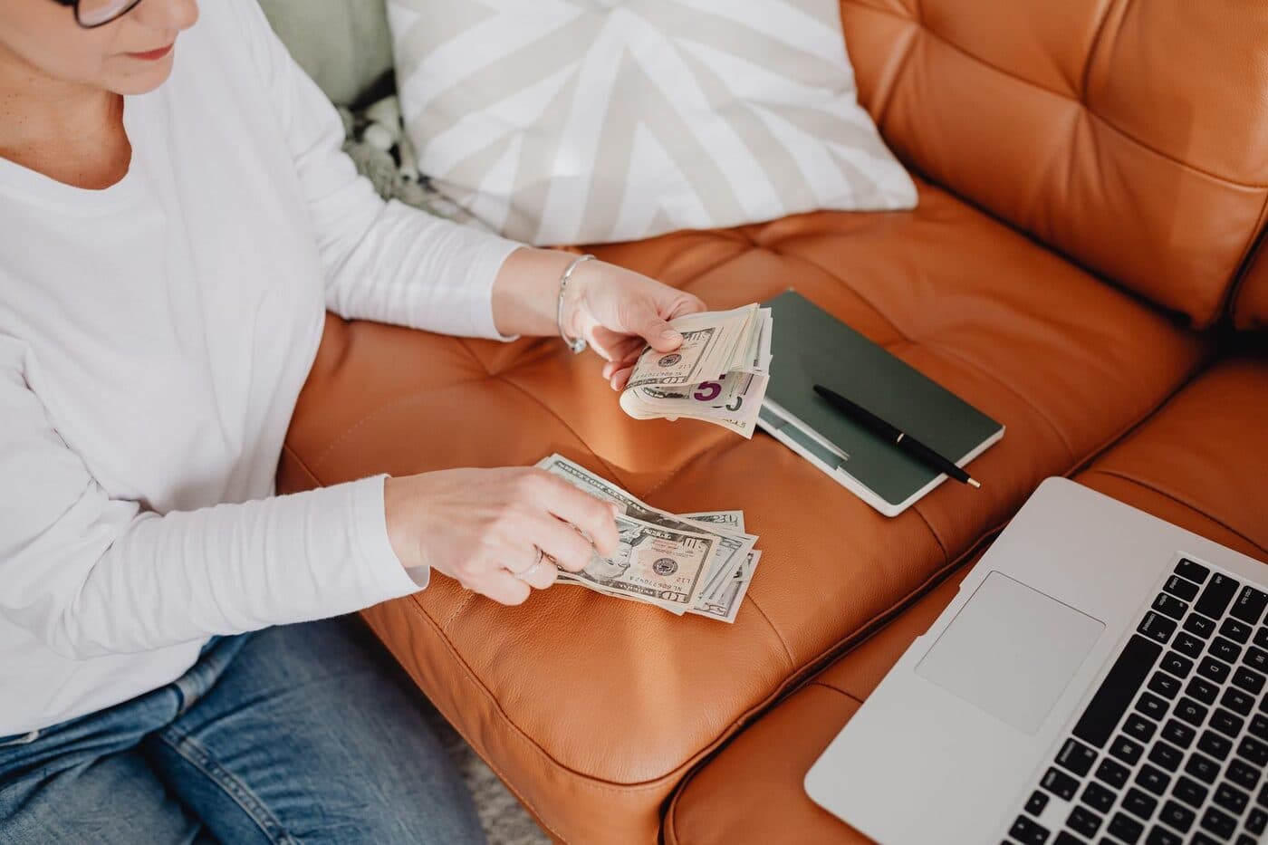 A person counting earnings while working on a laptop at home