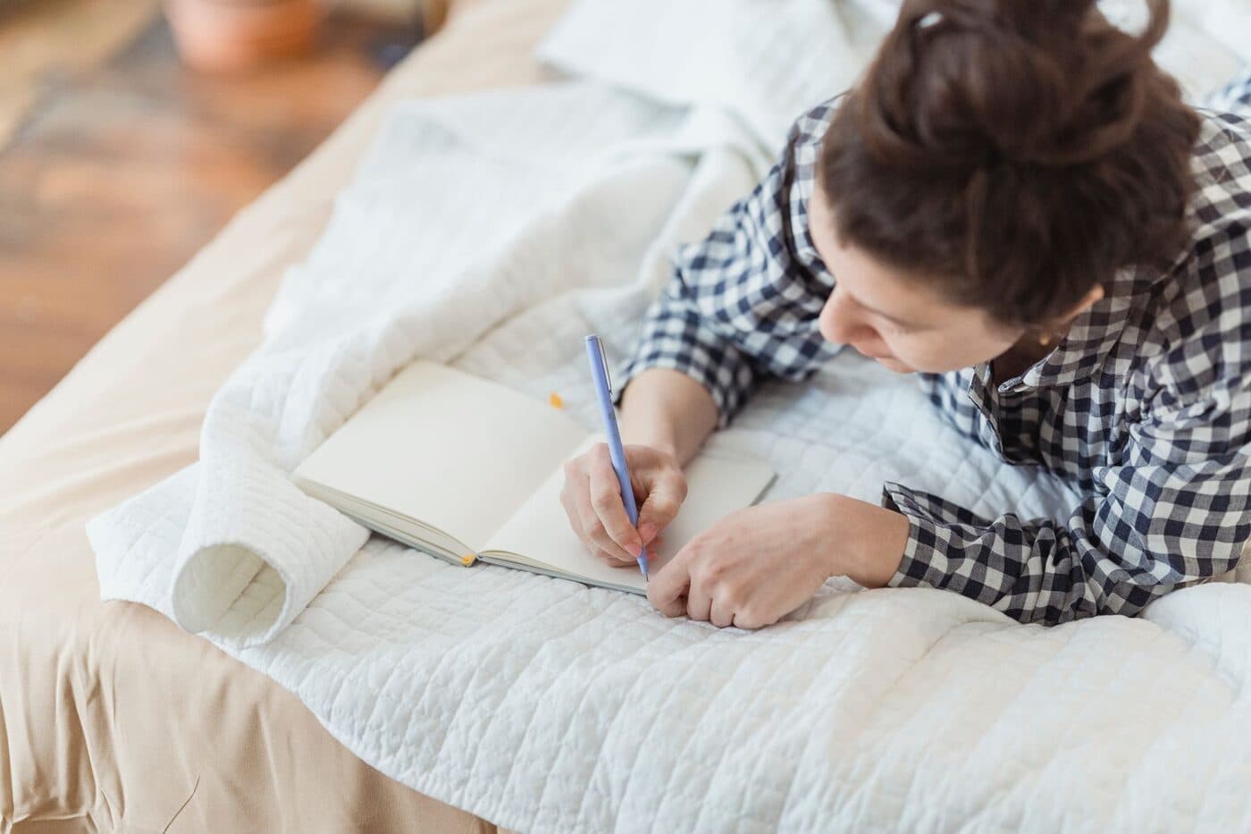 A blogger pausing to think while writing in a notebook beside a laptop